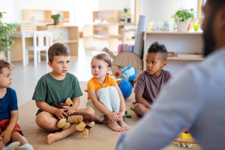 small group of preschool children sitting on the floor talking in a classroom