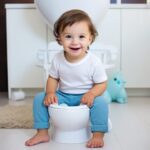 toddler boy sitting on white potty in bathroom wearing white t-shirt and blue pants.