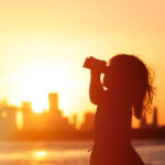 toddler uses binoculars to look into a urban environment at sunset