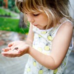 Blonde girl in dress holds small frog in hands