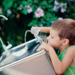 little boy reaching for a drink of water from a water fountain
