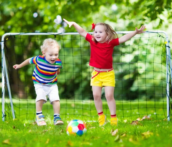 two happy kids playing soccer outside in front of a goal