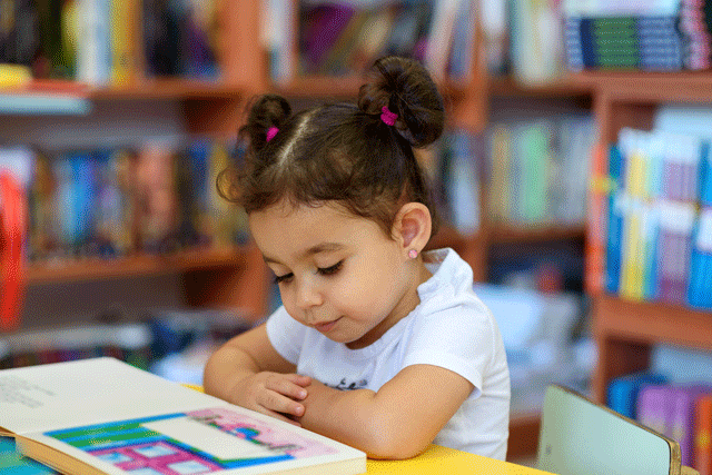 Little girl reading a book at a table