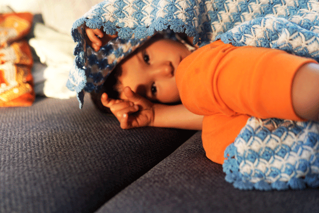 Child laying under a blanket on the couch