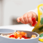 Toddler picking up a strawberry from a bowl of healthy food