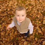 boy standing in leaves looking up at the sky