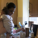 Mom holding infant making tea in the kitchen
