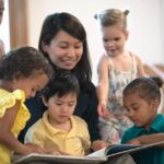 teacher smiling and reading a book to several toddlers