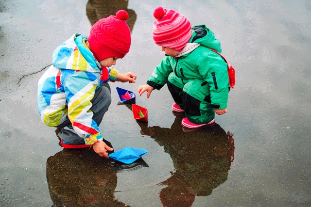 Children playing in a puddle with paper boats