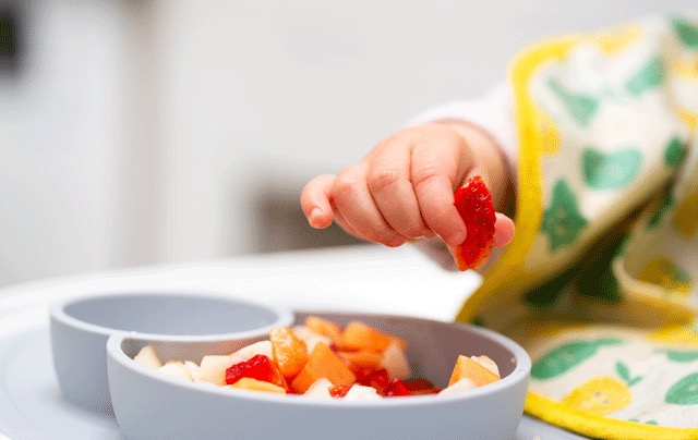 Toddler picking up a strawberry from a bowl of healthy food