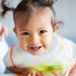 girl toddler smiling with bib and pigtails