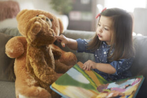 girl reading storybook to two teddy bears