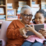 Smiling grandmother and granddaughter using digital tablet.