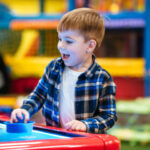 Cheerful little boy playing air hockey game at indoor playground