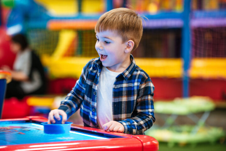 Cheerful little boy playing air hockey game at indoor playground