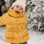 Toddler girl happy with snow day in winter, wearing a yellow coat and a hat
