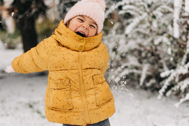 Toddler girl happy with snow day in winter, wearing a yellow coat and a hat