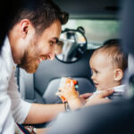 dad buckling toddler into car seat
