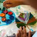 Child paints leaf on table